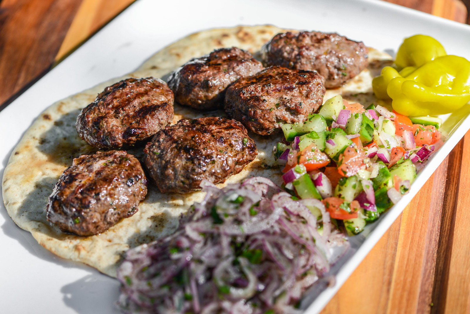 Grilled Turkish köfte meatballs served with sumac onions, peppers, and flatbread