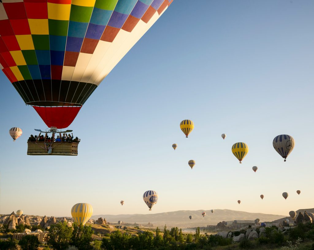 Hot air balloon basket with passengers and pilot operating the burner over Cappadocia at dawn