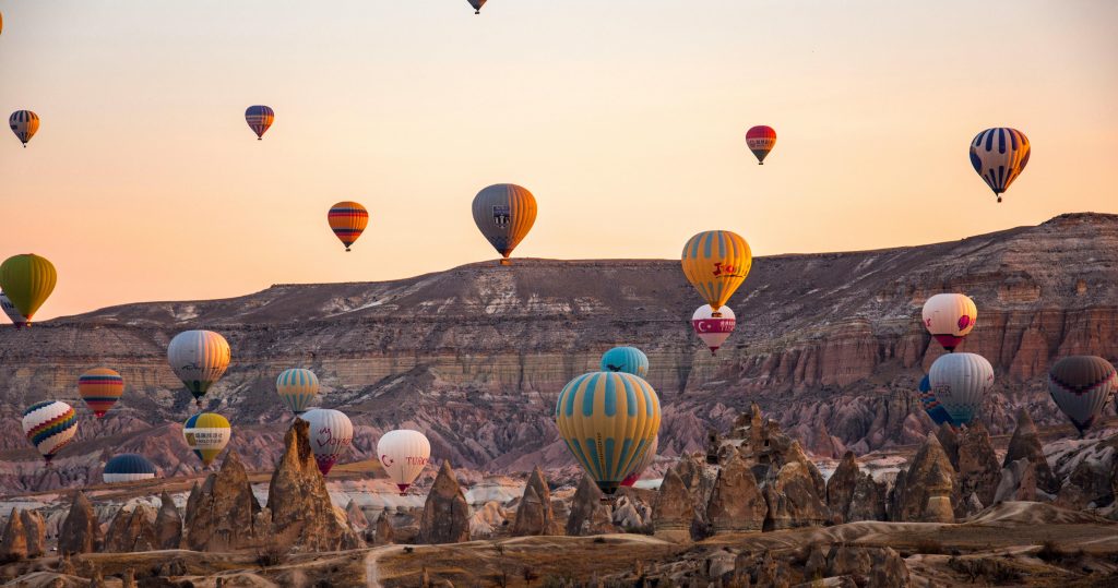 Cappadocia hot air balloons viewed from a free Rose Valley sunrise viewpoint with fairy chimneys in the foreground